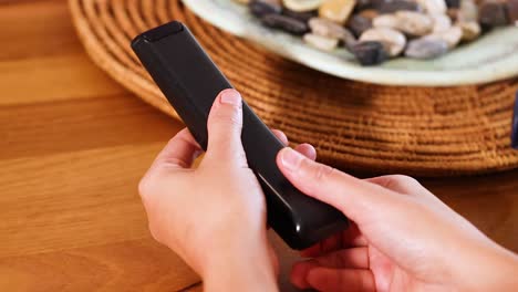 hands replace batteries in a remote control on a wooden table with natural lighting