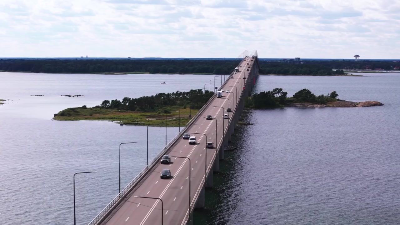 Volo laterale sopra il trafficato Ölandsbron, vista della parte superiore del ponte, della terraferma e di una piccola isola.