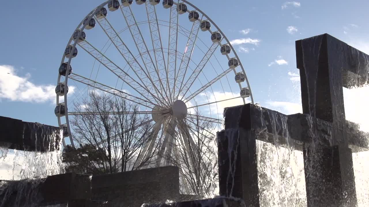A pigeon flies in front of the fountain at Seattle's Waterfront Park at sunset. The Seattle Great Wheel turns in the background. Slow motion. Filmed in 2013.