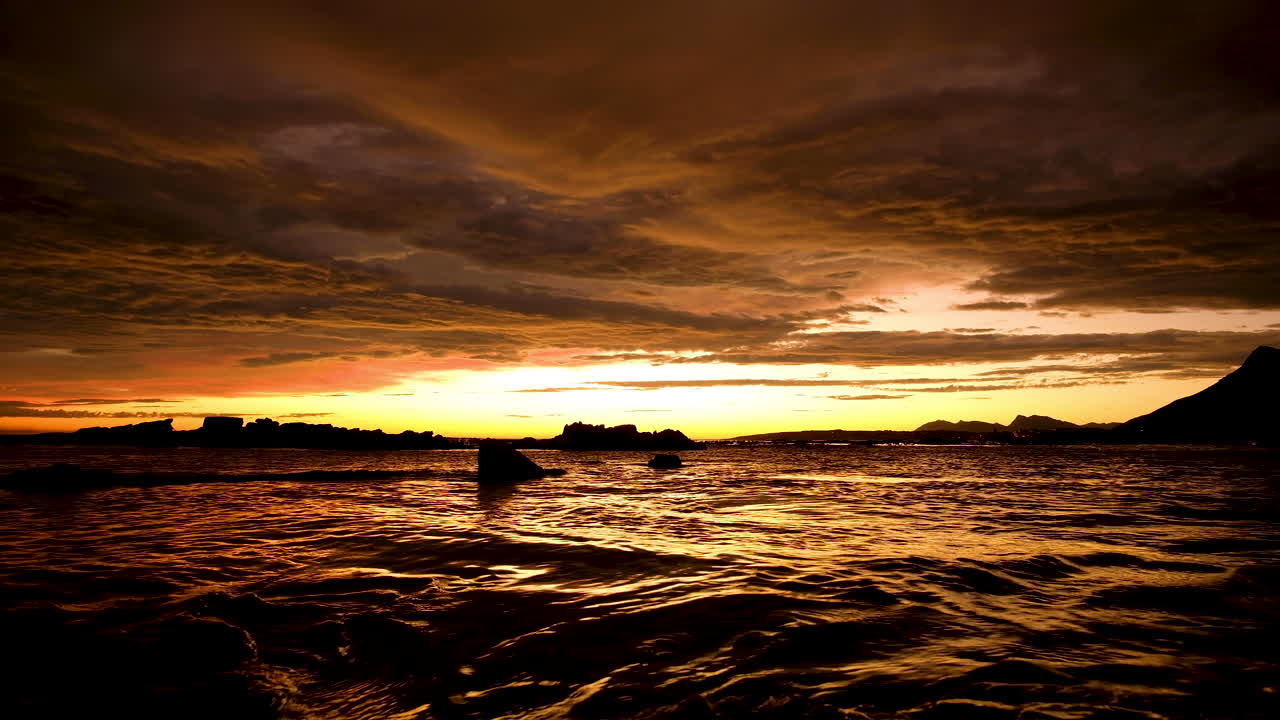 puesta de sol de fuego sobre el océano, paisaje de nubes iluminado en naranja, superficie de mar de oro líquido