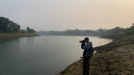 photographer shooting polluted river scene on misty day with camera, static