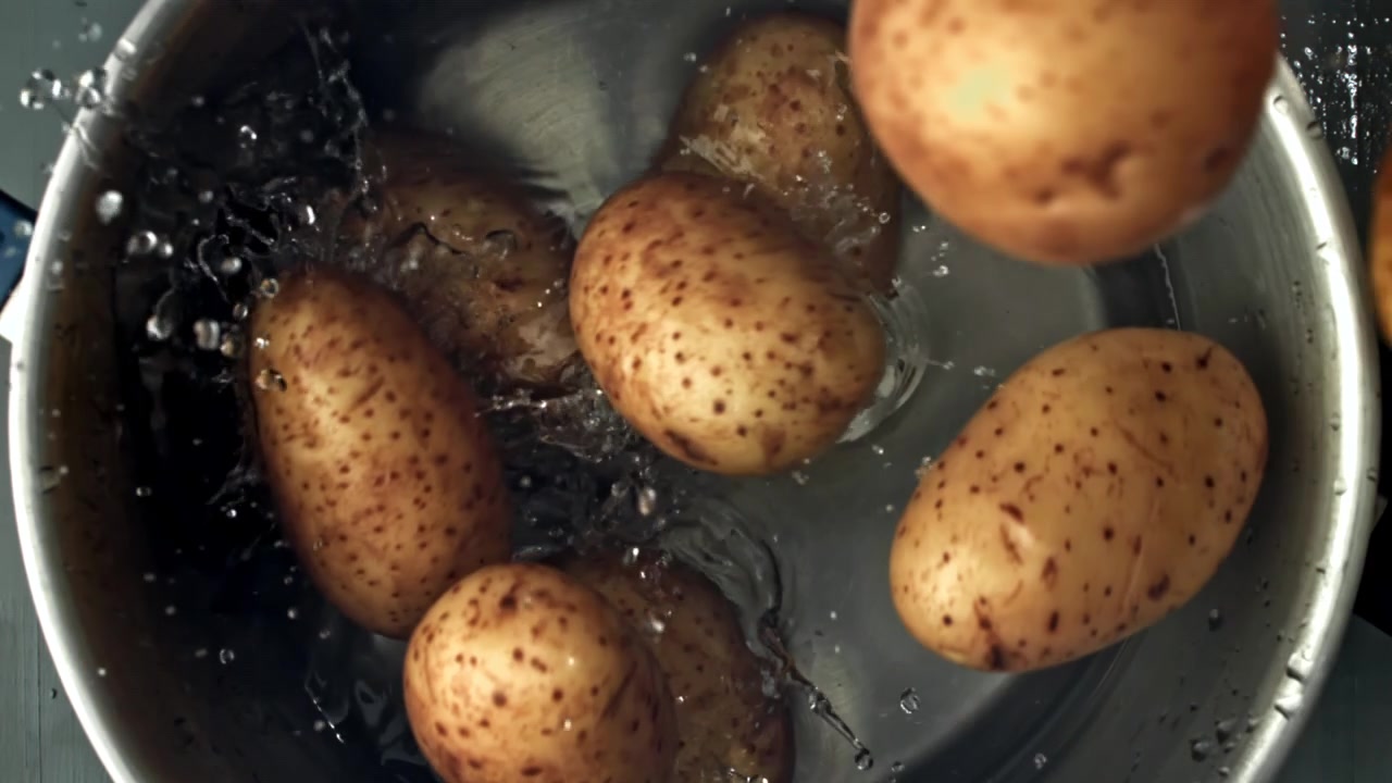 Patate fresche che schizzano nell'acqua in una pentola di metallo al rallentatore