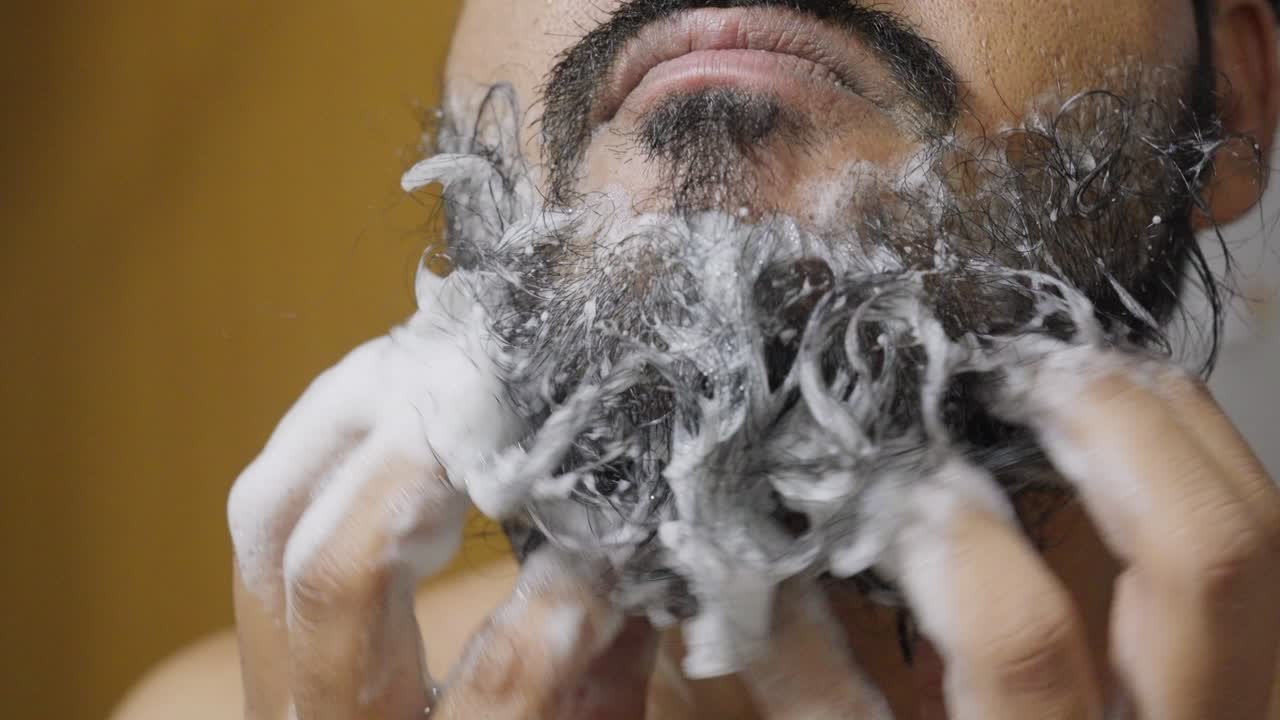A closeup footage of a South Asian man rubbing his beard with soap and water, with blurred background