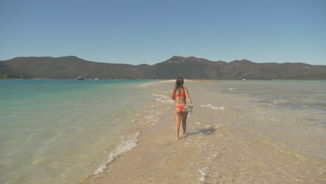 Back-View-Of-Female-Snorkeler-With-Snorkeling-Gears-In-Hand-Running-On-Sand-Bar-In-Langford-Island,-Australia