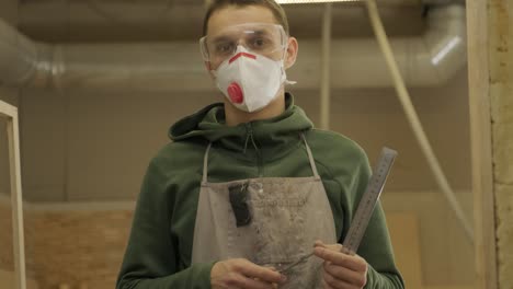 portrait of worker carpenter with respirator and glasses in workshop, holds the ruler