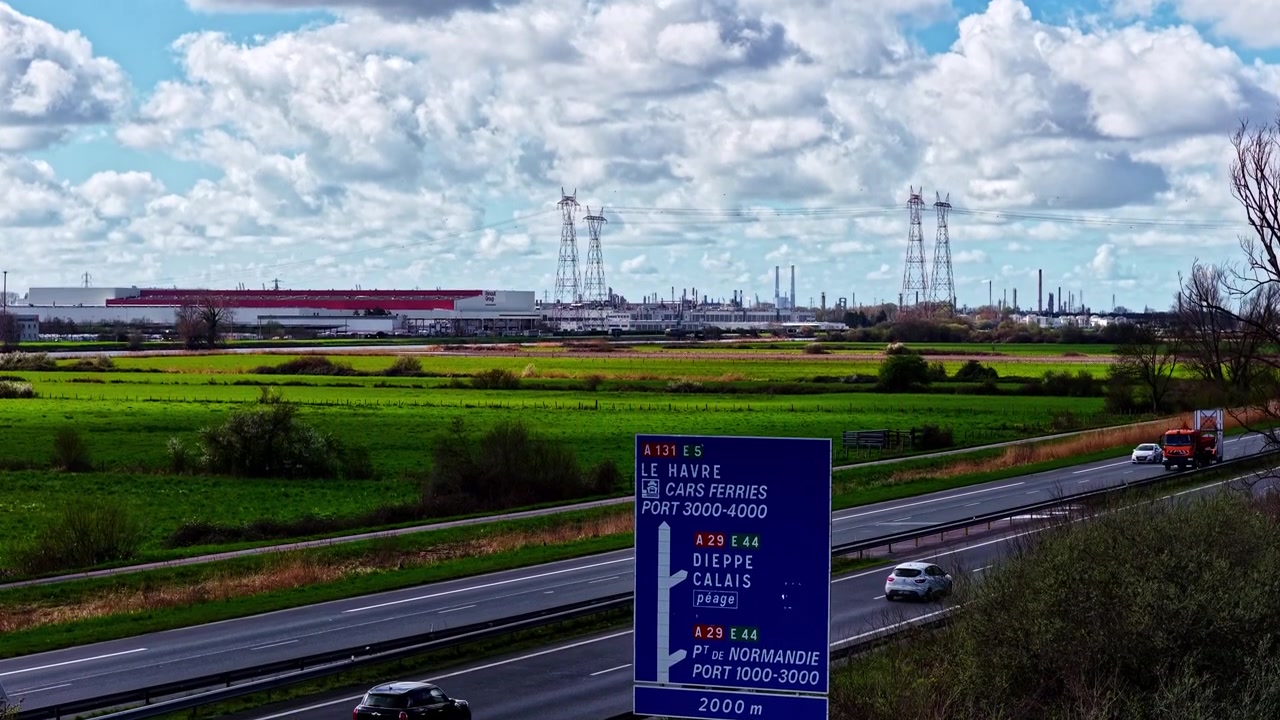 Verkehrsschild an einer Autobahn mit bewölktem Himmel und entfernten Windrädern im Hintergrund