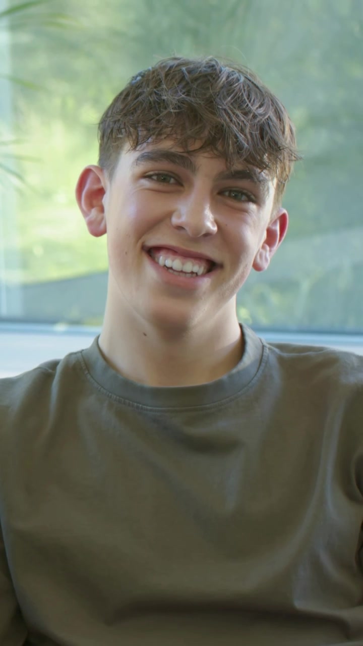 Ragazzo adolescente seduto sul divano vicino alla finestra, che risponde a qualcuno fuori campo, sorridendo per marketing.