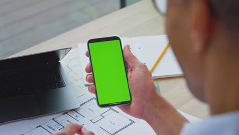 Close-Up-Of-Mature-Male-Architect-Working-On-Laptop-In-Office-At-Desk-Browsing-On-Mobile-Phone