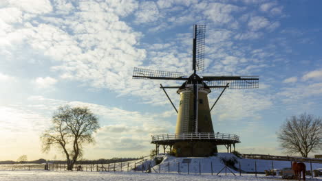 Time-lapse-of-clouds-passing-over-traditional-windmill-in-beautiful-white-winter-rural-landscape---pan-left-to-right