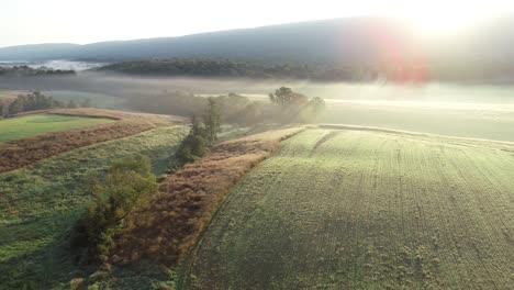 aerial camera moving to the right showing farm fields, trees, mountains, and fog in the morning light