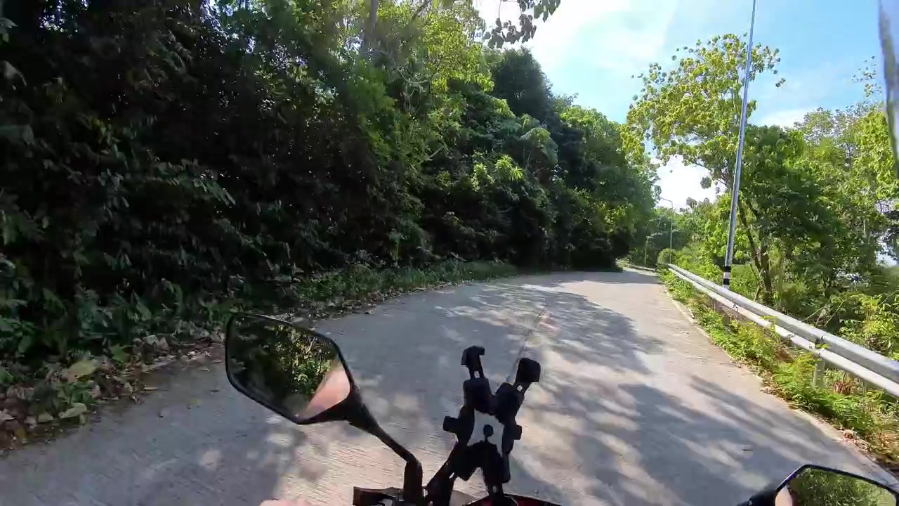 Viaggio in moto lungo una tranquilla strada tropicale circondata da un lussureggiante paesaggio della giungla sull'isola di Koh Lanta in Thailandia.