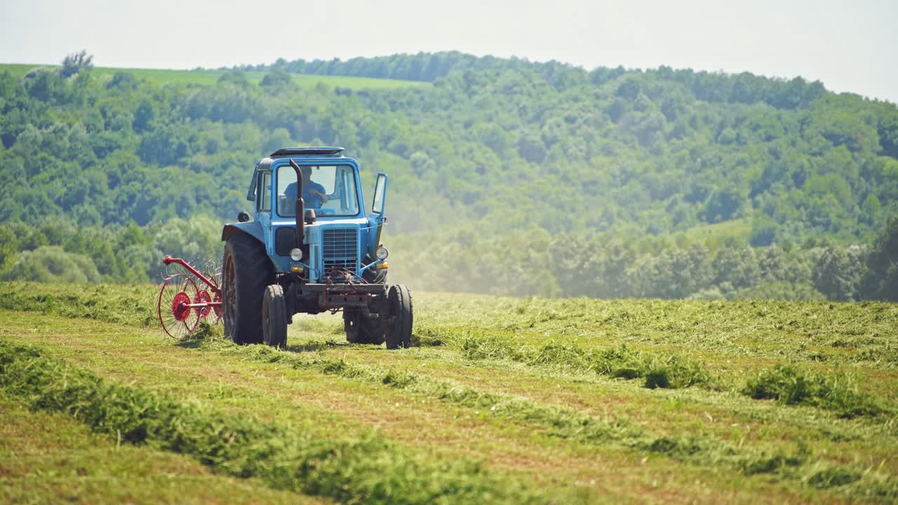 Front view of a tractor working on the field in summer. Agricultural machine changing dried grass on the natural field background.