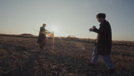 couple preparing to fly colorful kite in open field during golden sunset