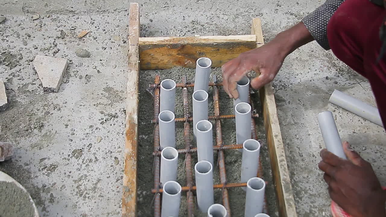 Indian mason worker placing PVC pipes in steel mesh for construction reinforcement in a cement mold