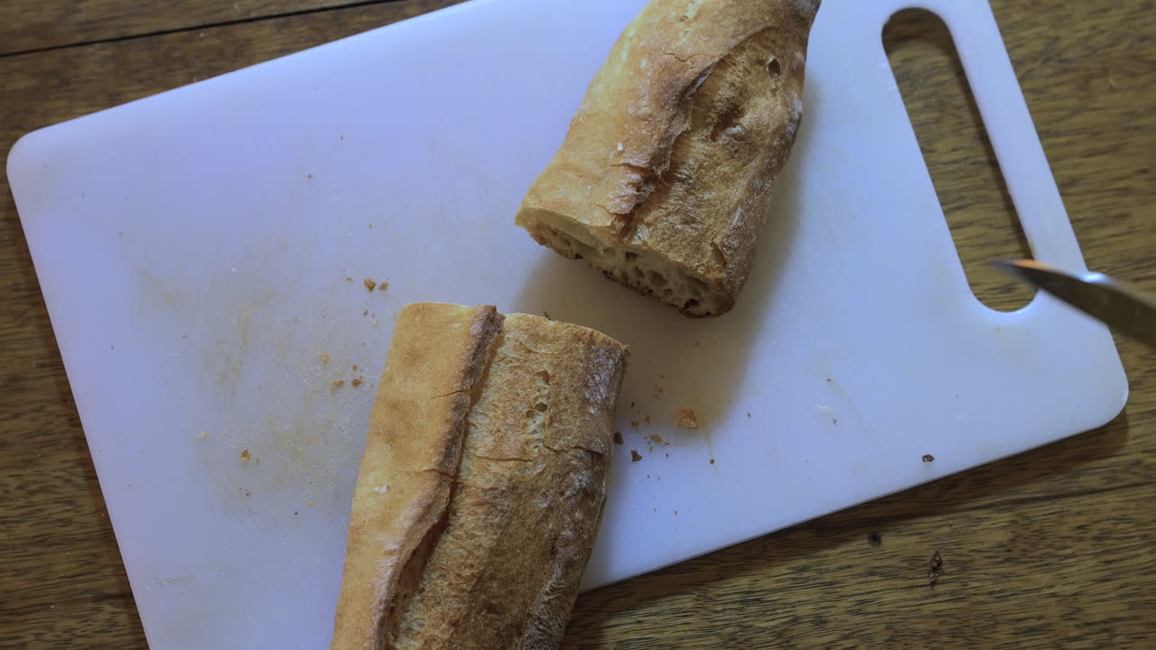 흰색 커팅 보드에 프랑스 바게트를 반으로 자르는 백인