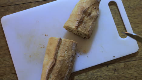 hombre blanco cortando por la mitad una baguette francesa en una tabla de cortar blanca