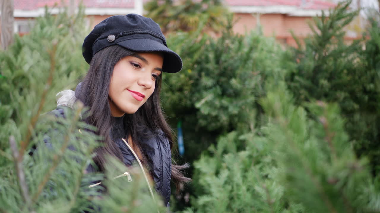 una mujer hispana comprando una decoración navideña de temporada en un lote con muchas especies de árboles festivos