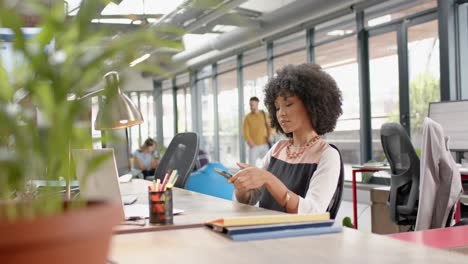 african american woman using smartphone sitting on her desk at office