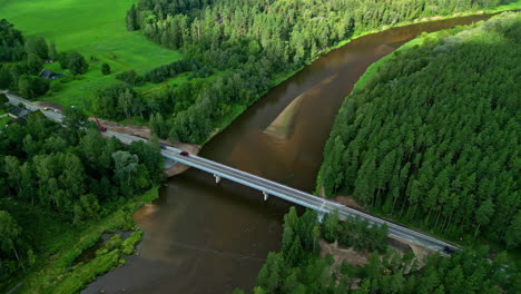 Vista-Aérea-De-Un-Puente-De-Hormigón-Sobre-Un-Río-Que-Fluye-Entre-Bosques-De-Coníferas