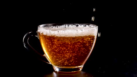 Tea is poured into a glass cup against a black background, highlighting the liquid's motion and bubbles