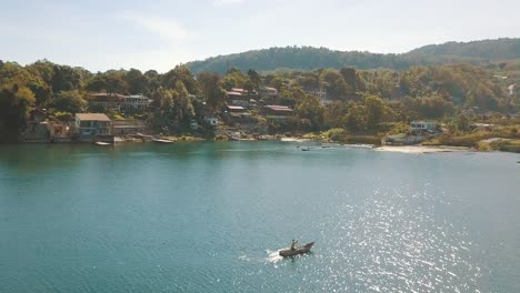 drone aerial flying over a fisherman paddling on a boat in lake atitlan, guatemala