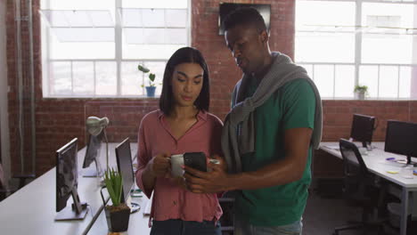 Diverse-male-and-female-business-colleagues-in-discussion-at-work-using-smartphone-holding-cups