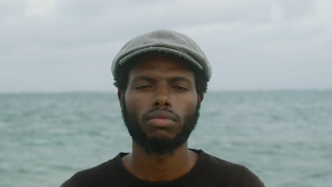 shaky close-up of a young black african man looking at a camera with a serious face and the ocean in the background