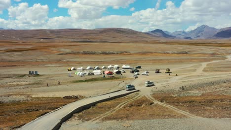 Drone-Aéreo-De-Camionetas-Que-Transportan-Carga-Y-Turistas-Que-Llegan-A-Un-Campamento-En-La-Llanura-Alpina-De-Gran-Altitud-Del-Parque-Nacional-Deosai-Ubicado-Entre-Skardu-Y-El-Valle-De-Astore-En-Pakistán-En-Un-Día-Soleado