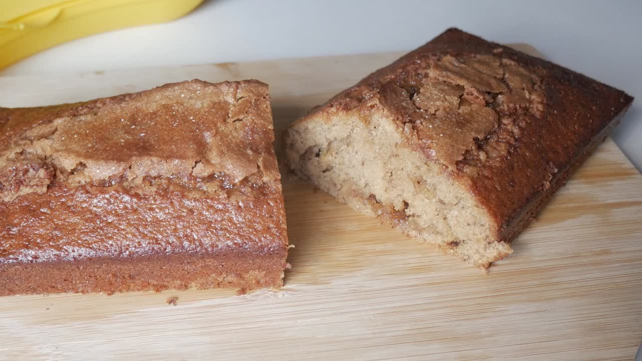Zoom out shot of banana bread loaf cut open on wooden board, showing moist crumb and crust