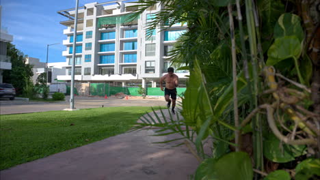 Slow-motion-panning-of-a-young-hispanic-man-shirtless-sprinting-in-front-of-the-camera-on-a-bright-sunny-day