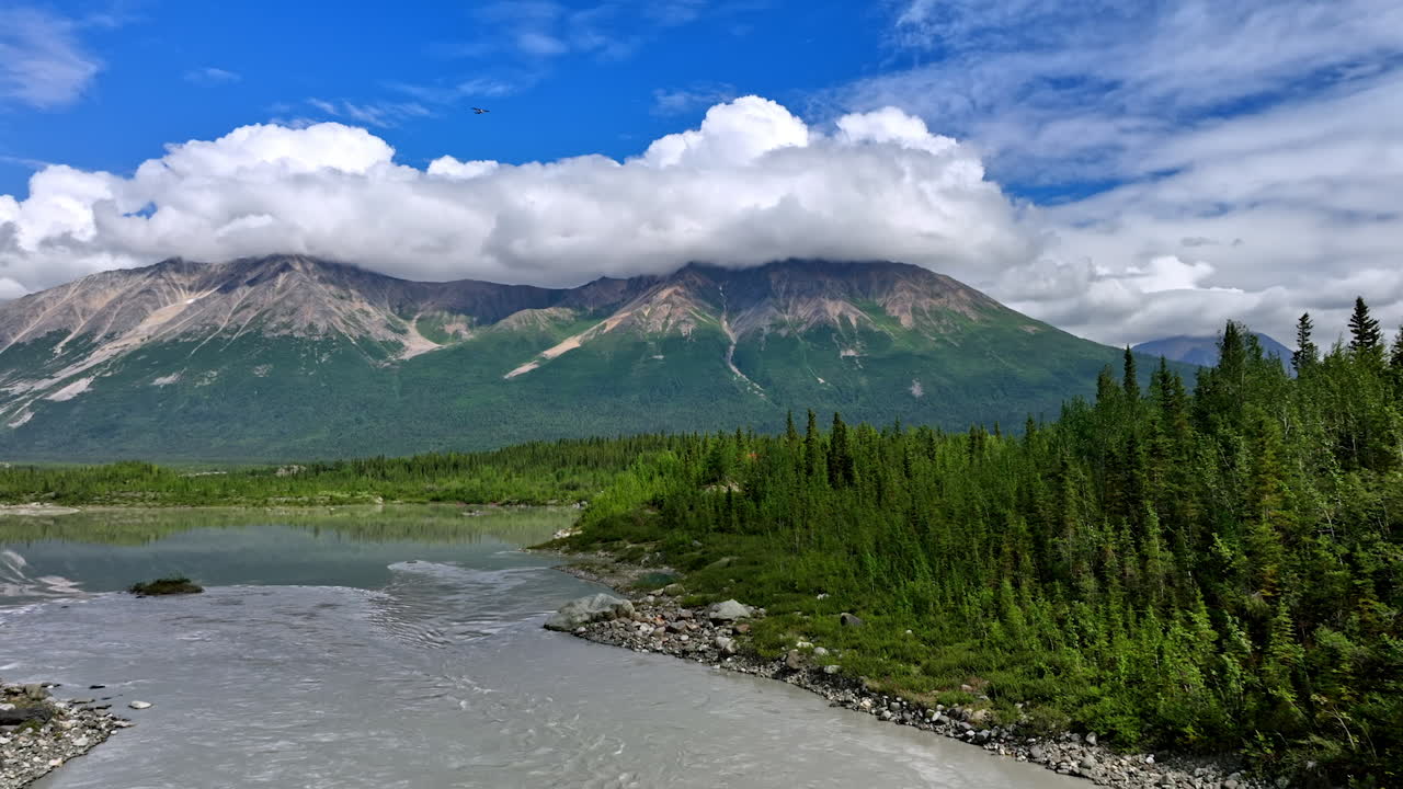 Paesaggio aspro mozzafiato dell'Alaska. Montagne maestose si ergono sopra valli verdi e vivaci e un fiume sereno sotto un cielo azzurro brillante in Alaska.