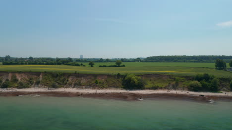 Aerial-drone-view-of-vast-springtime-green-countryside-field,-Baltic-sea,-Brodten,-Germany,-backwards,-sunny-day