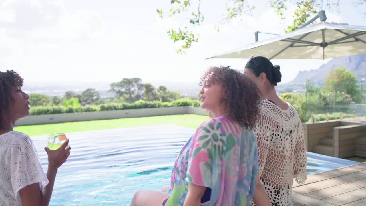 African-American women friends talking, toasting at infinity-pool deck, phone nearby, view sparking