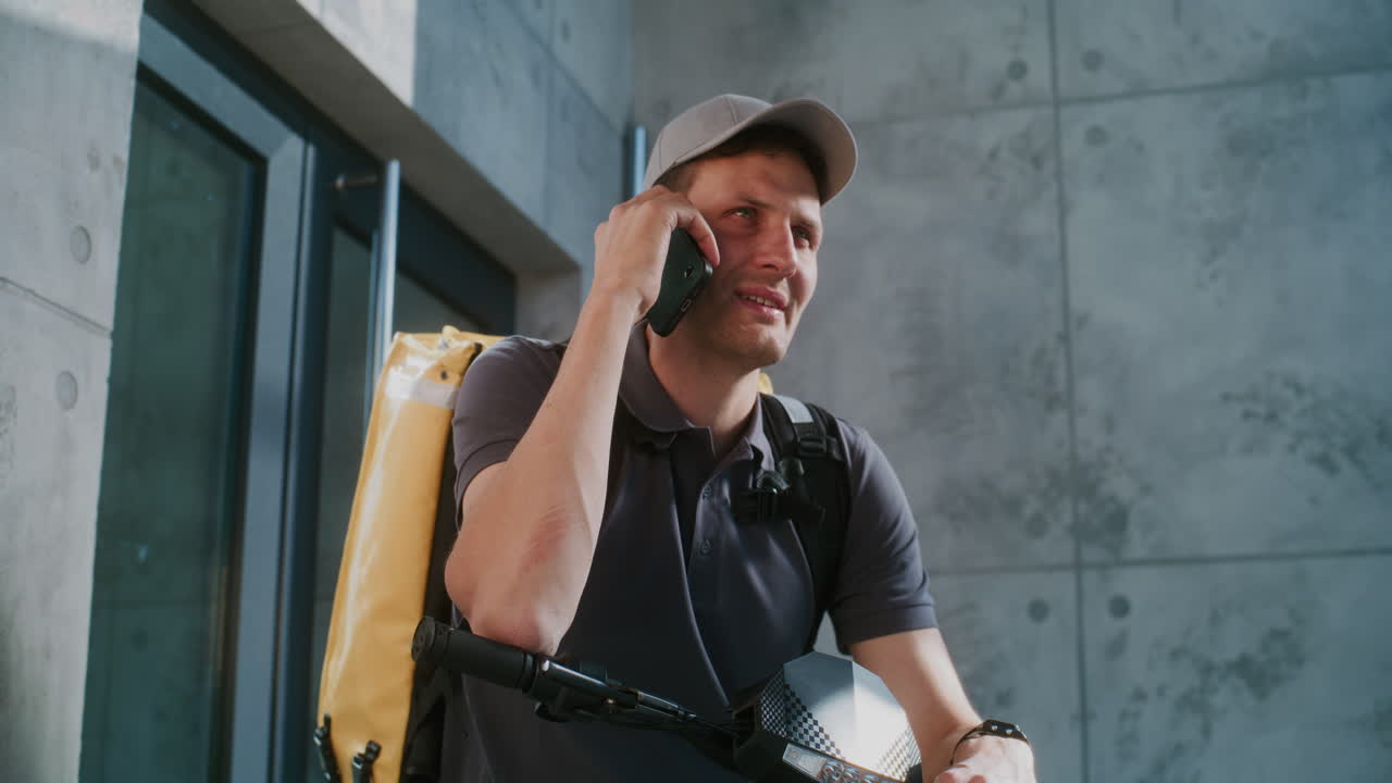A delivery person on a scooter talking on a smartphone outside a modern building