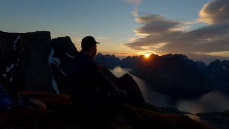 Hiker-enjoying-the-breathtaking-view-during-midnight-sun-at-the-worlds-famous-peak-Reinebringen-in-Lofoten