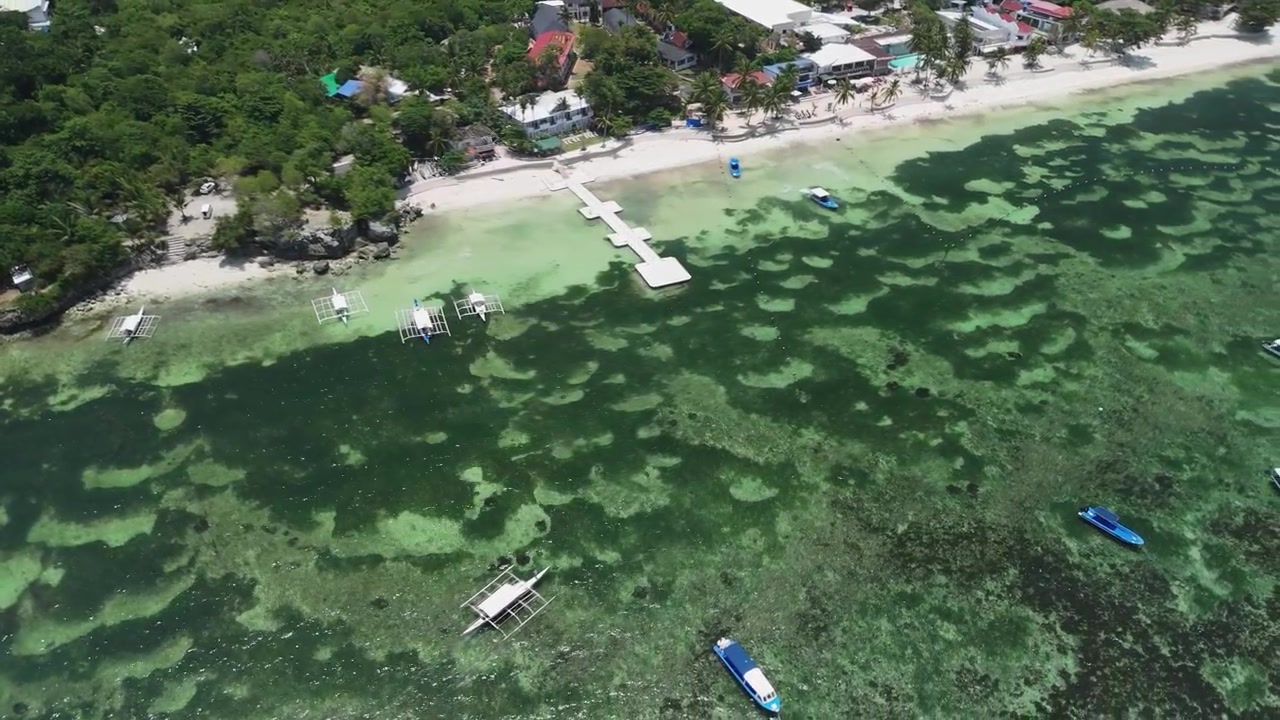 Drone con ripresa dall'alto che orbita barche in partenza da Alona Beach e che navigano attraverso acque poco profonde della barriera corallina lungo la costa di Panglao a Bohol