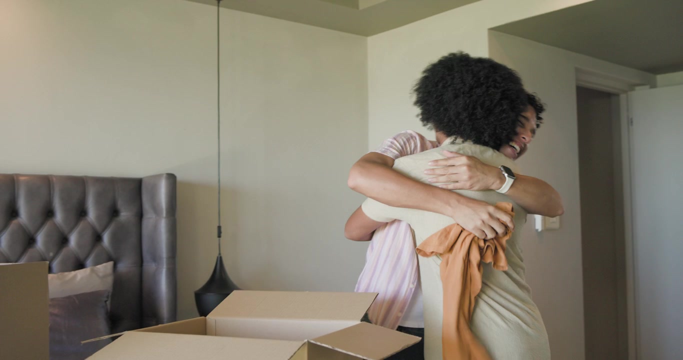Duo maschile multietnico che si prepara a traslocare in camera da letto, piegando una maglietta arancione, controllando il telefono e impacchettando una scatola per donazioni.