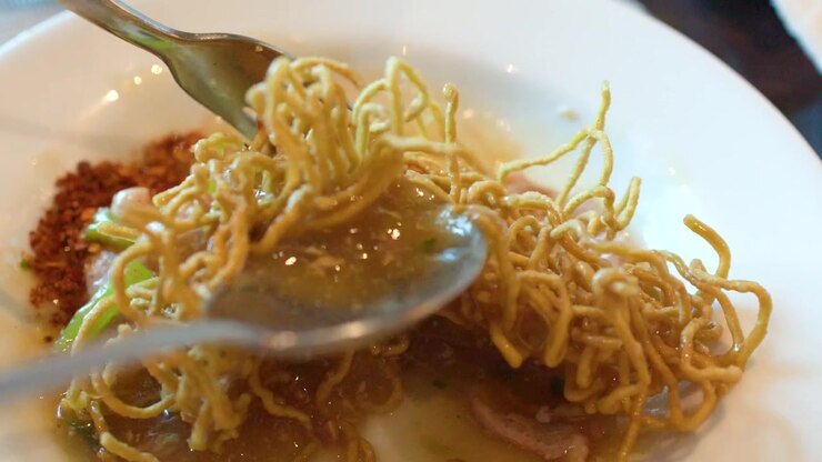 Primo piano di una persona che mescola noodles all'uovo croccanti e maiale in una saporita salsa thailandese.