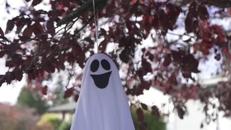 Primer-Plano-De-Seguimiento-De-Una-Espeluznante-Decoración-Fantasma-De-Halloween-Colgando-De-Un-árbol-En-Flor-En-Otoño-Y-Balanceándose-Con-El-Viento