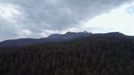Aerial-footage-of-a-cloudy-forest-and-a-vast-mountain-range-in-the-background