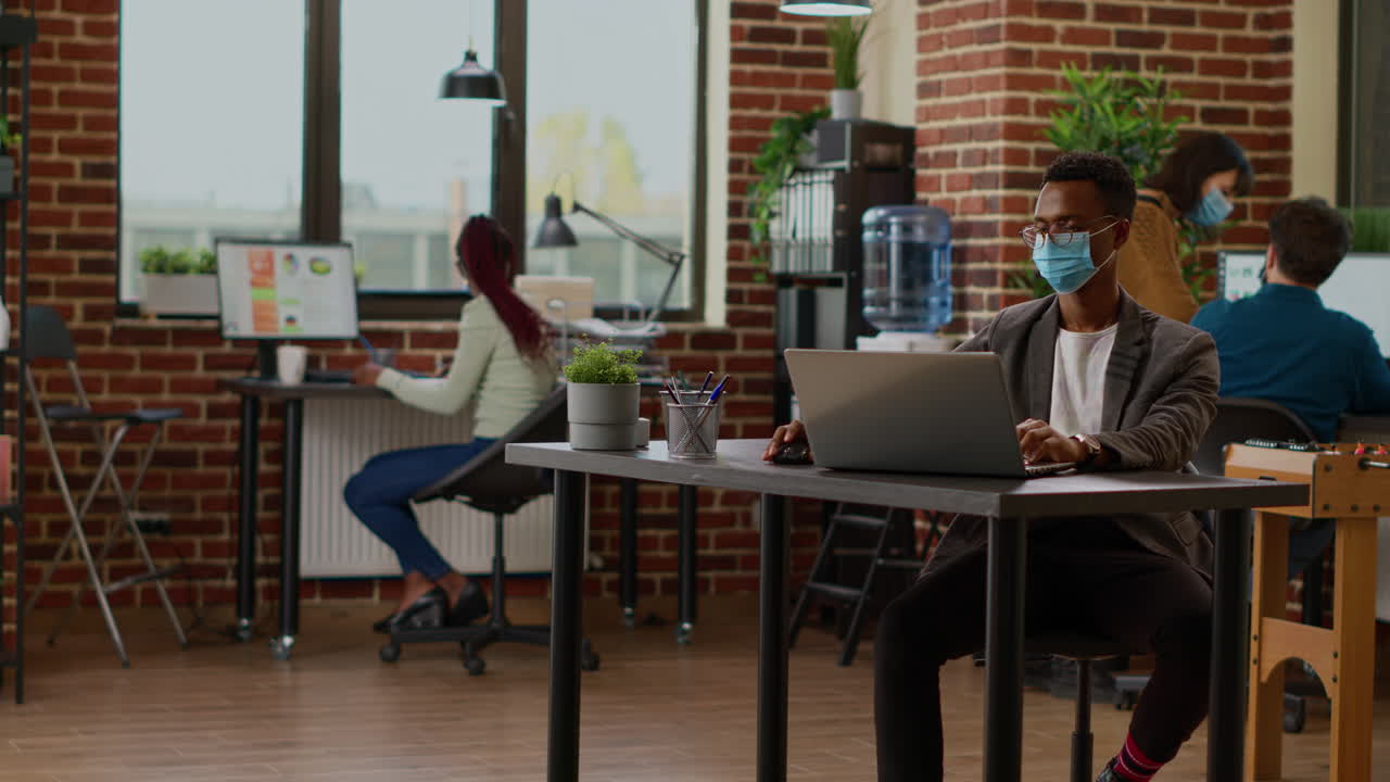 Project manager with face mask working with data on laptop