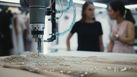 in a contemporary workshop, fashion designers focus on creating exquisite garments. a high-tech machine intricately embellishes fabric with stunning details, showcasing creativity and innovation.