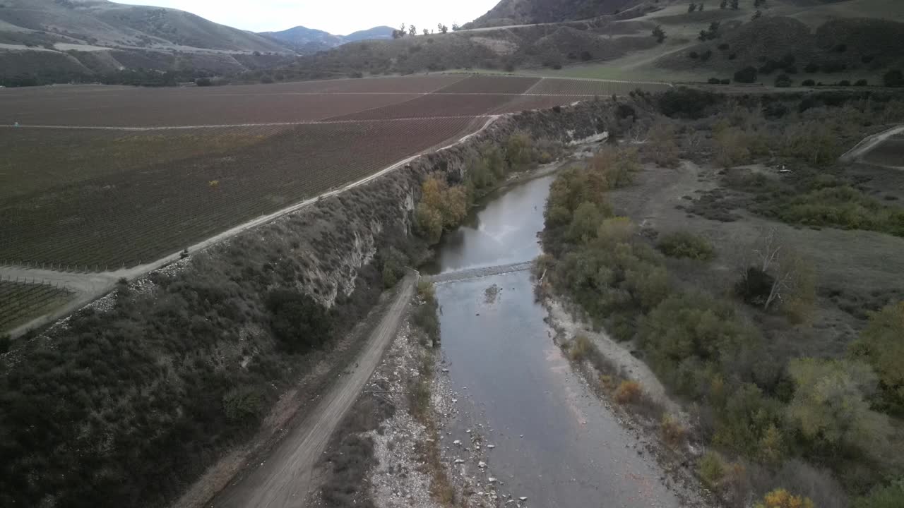 scatto aereo in discesa sopra il fiume arroyo seco che si snoda attraverso i vigneti e le fattorie di greenfield, in california, mostrando l'incrocio tra natura e agricoltura nella valle di salinas