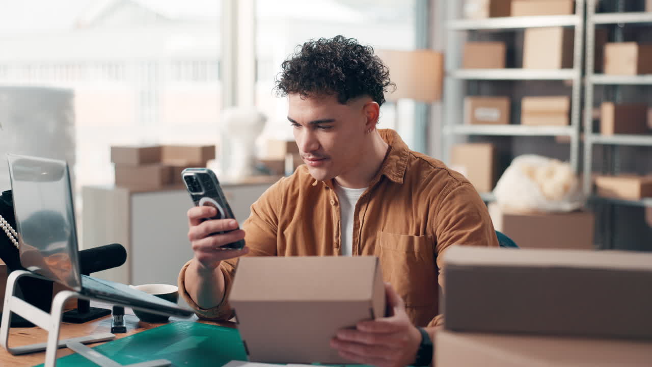 Man in office packing cardboard box and using cell phone