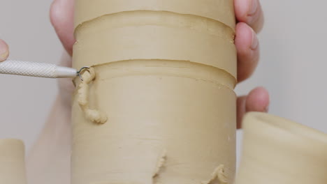 close-up of a hand carving clay with a pottery tool