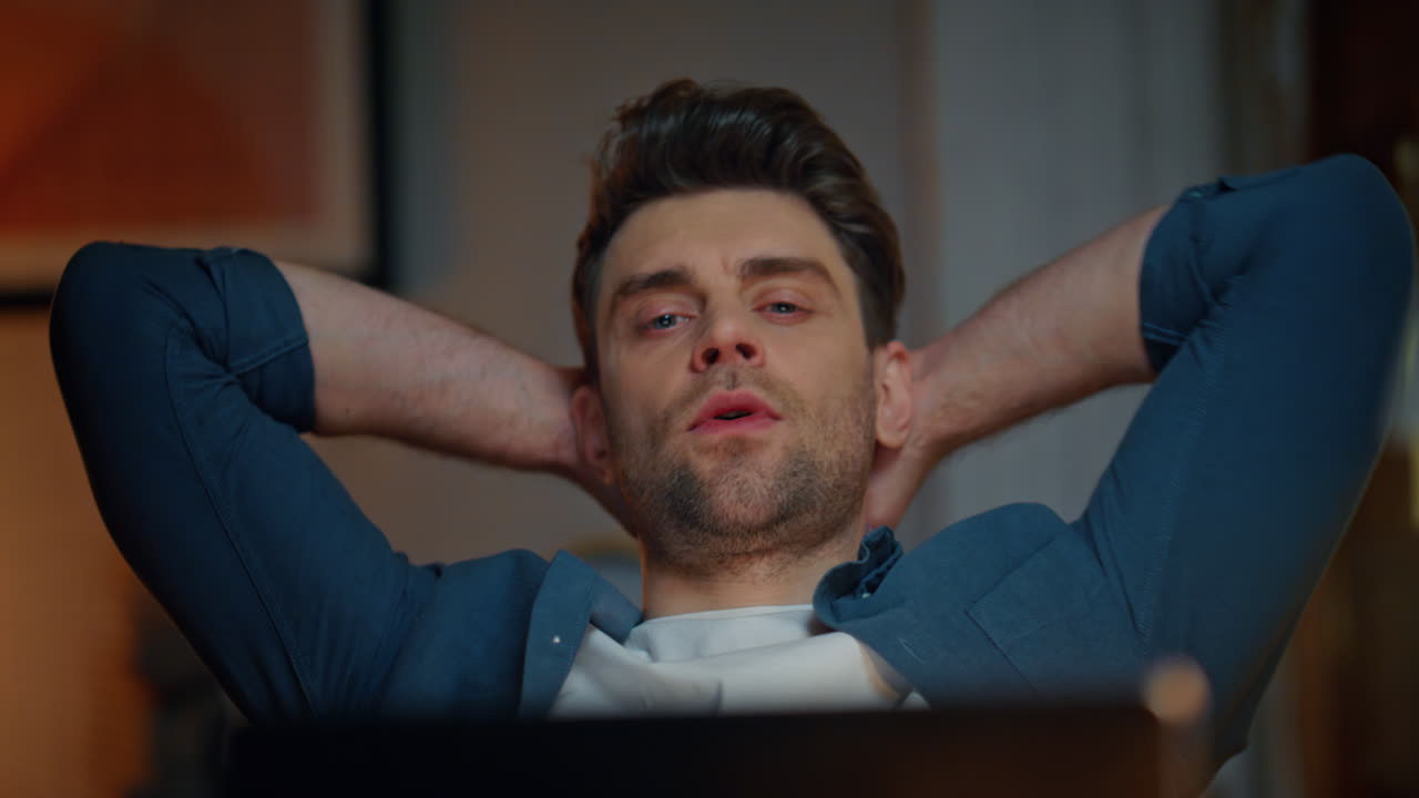 Relaxed man looking laptop at night workplace closeup. Guy stretching arms alone