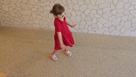 portrait of a 3 years old kid wearing red dress and eyeglasses dancing happily