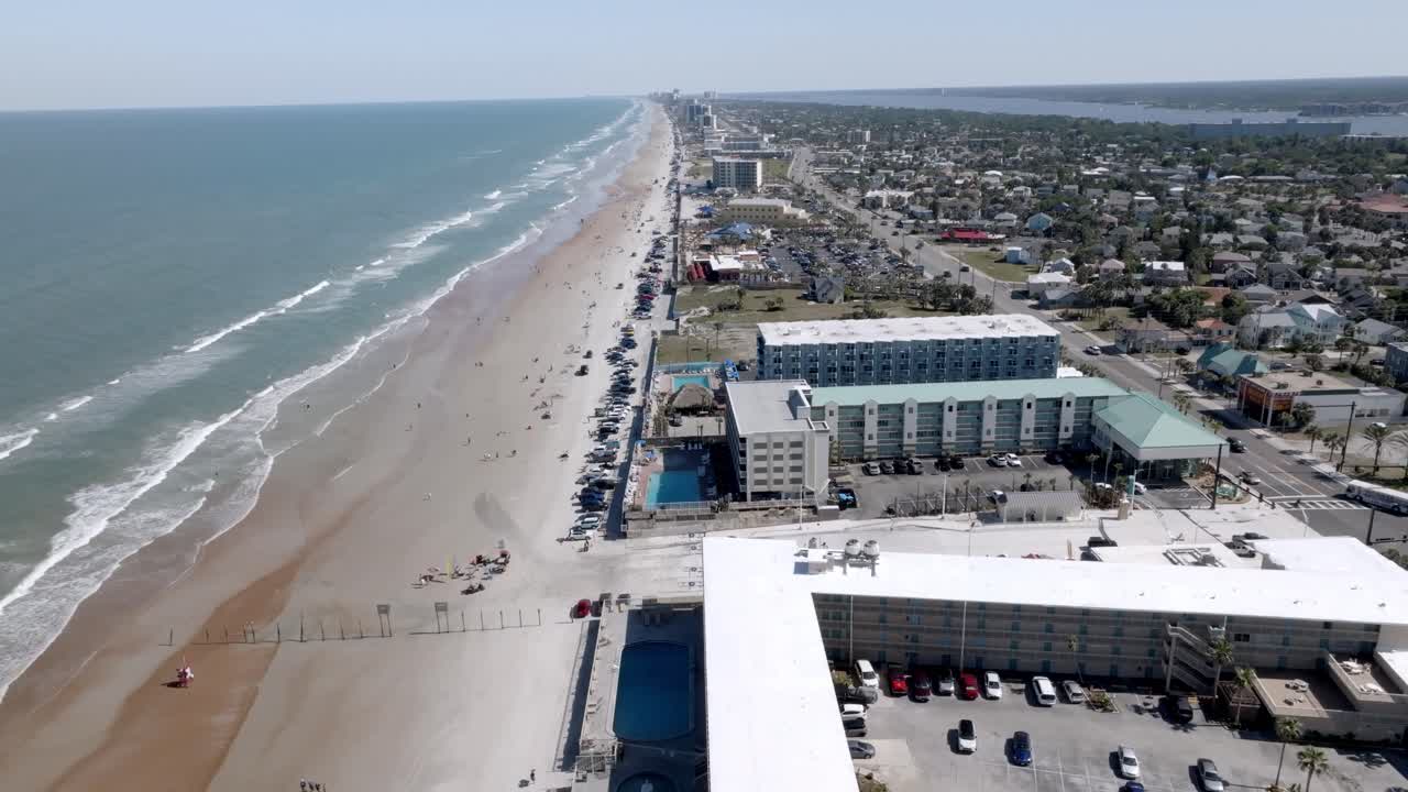 Daytona Beach, Florida with waves from the Atlantic Ocean, vehicles, hotels and people on the beach with drone video wide shot stable.