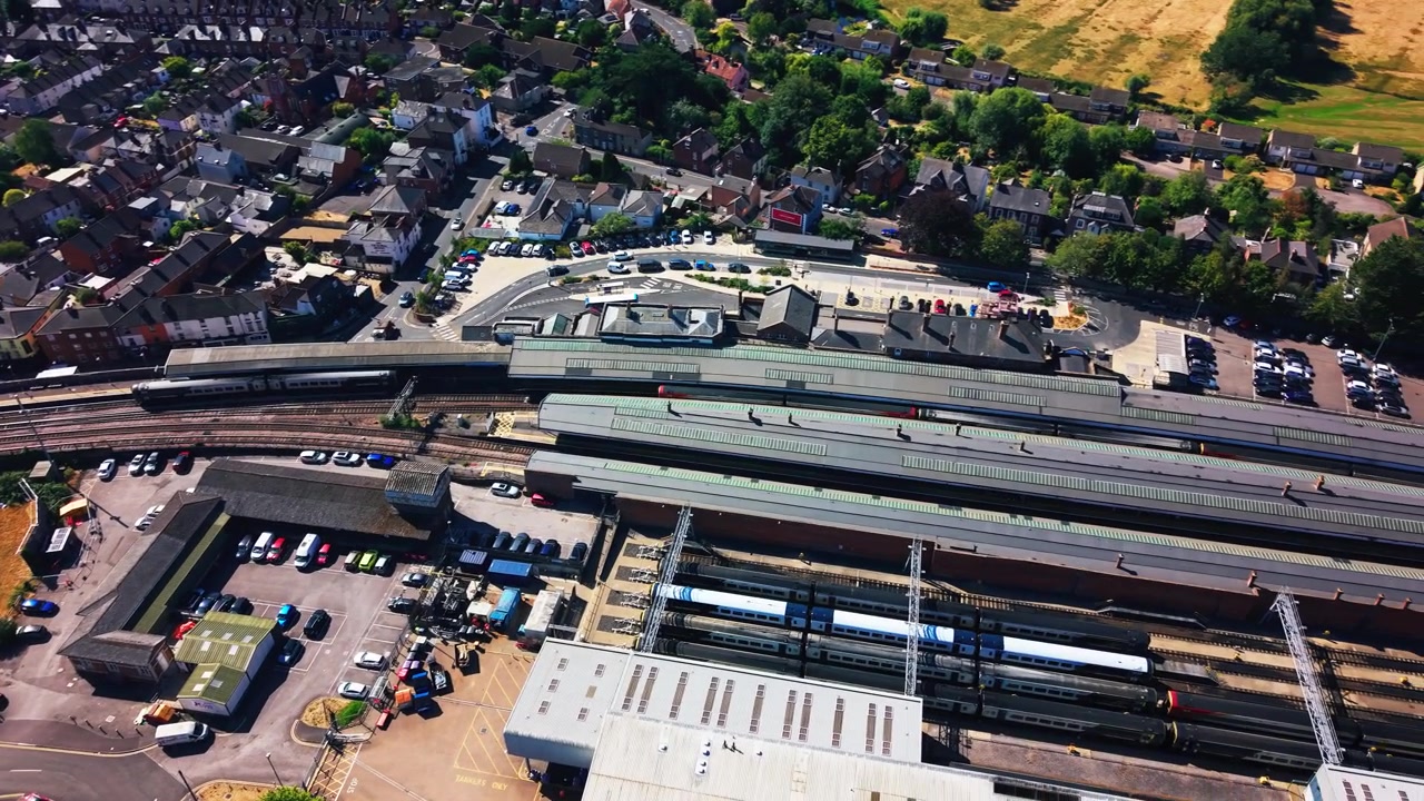 Højt luftfoto over Salisbury banegård, der viser passagertog, perroner, jernbanespor og omkringliggende gader i Wiltshire, England