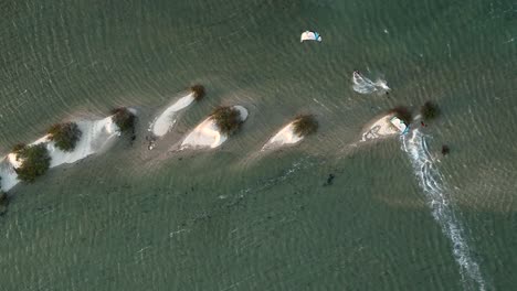 Zwei-Kiteboarder-Springen-über-Kleine-Dünen,-Die-Halb-In-Einer-Lagune-Versunken-Sind